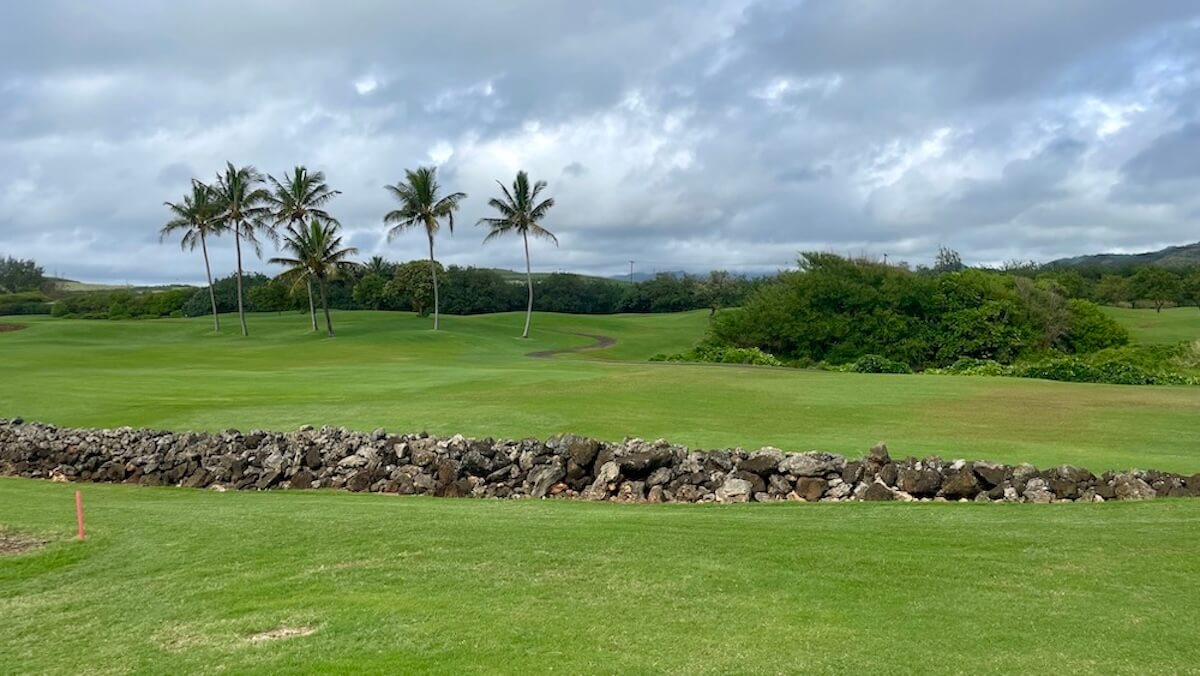 Poipu Bay Golf Course with palm trees and a rocky wall on a cloudy day
