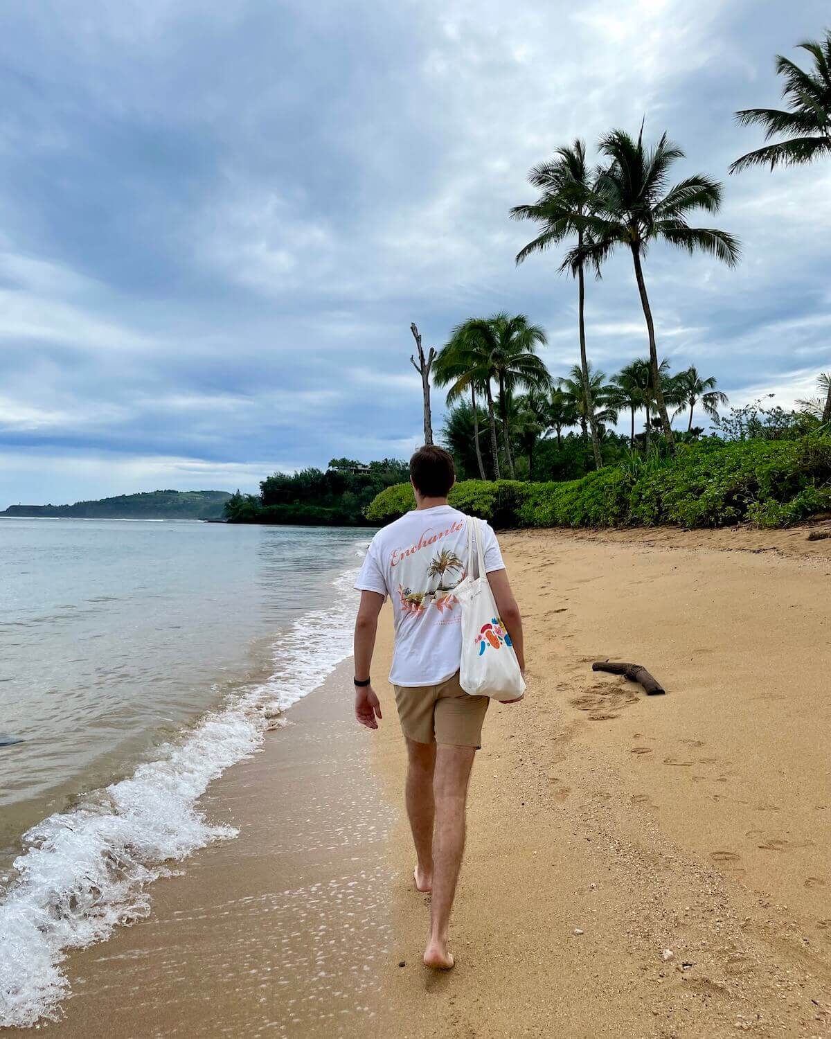 Lucas walking along water's edge on Anini Beach on partly-cloudy day in Kauai