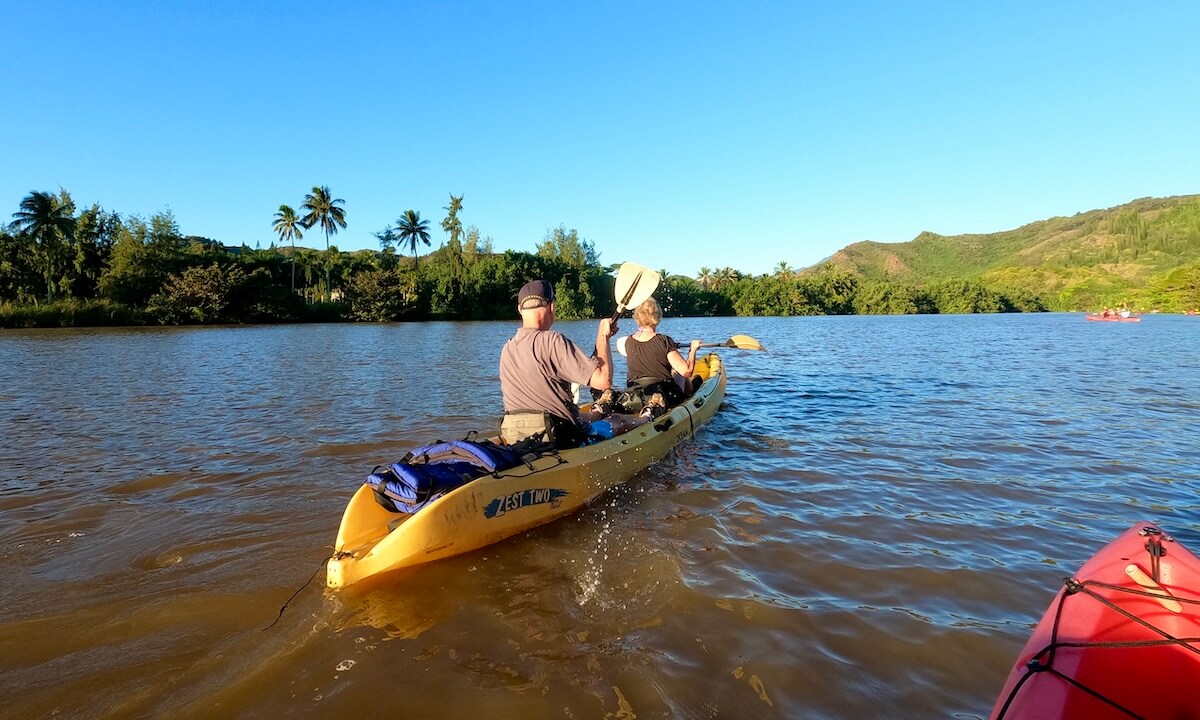 2 people kayaking along Wailua River with red paddles with lush Kauai landscapes