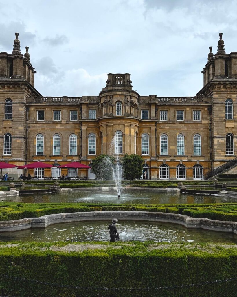 Blenheim Palace building and manicured ponds and fountain on cloudy day