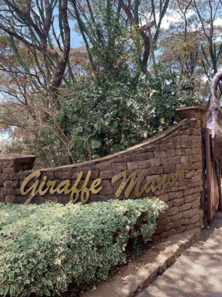 Giraffe Manor entrance gates with name written on brick wall and trees