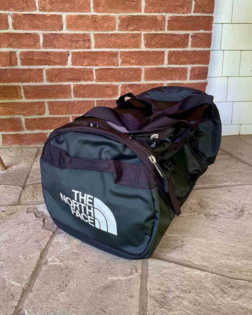 The North Face duffle bag in black on concrete floor against brick wall