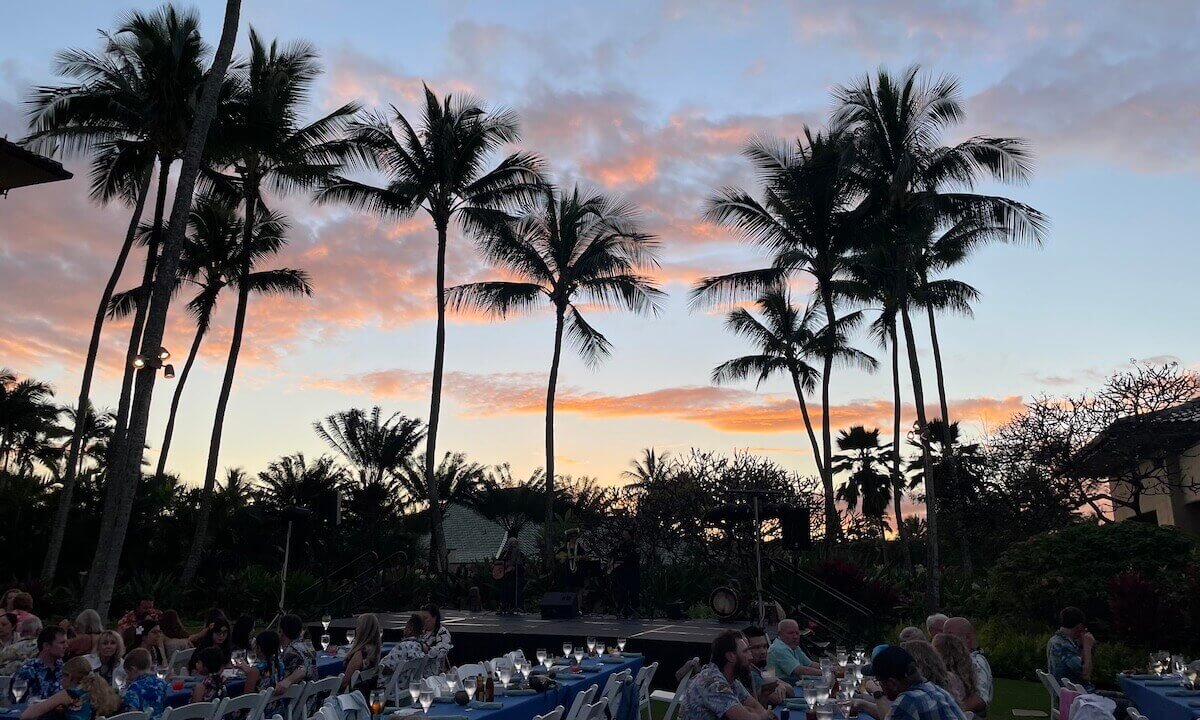 Palm trees and sunset in Grand Hyatt Kauai Luau with long tables seating people eating