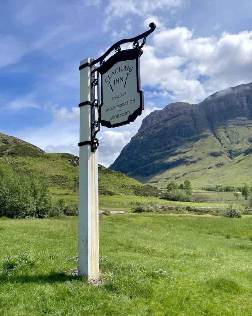 Clachaig Inn Glencoe signpost in front of huge mountain drop and grassy field