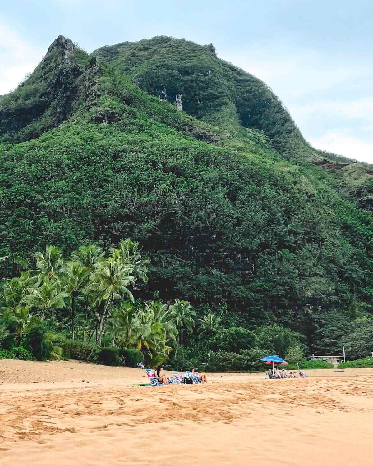Sunbathers on beach chairs on sand at Haena Beach with forested area and dull sky in Kauai