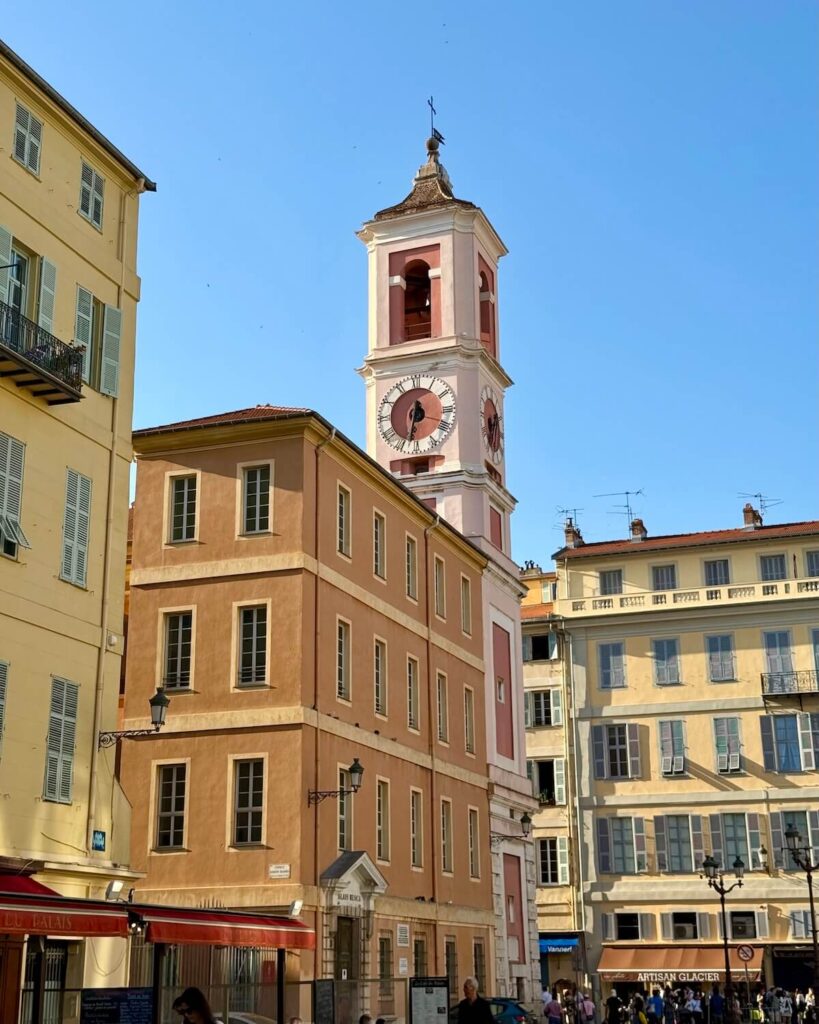 Old town of Nice with orange buildings and pink clock tower, with bright blue sky