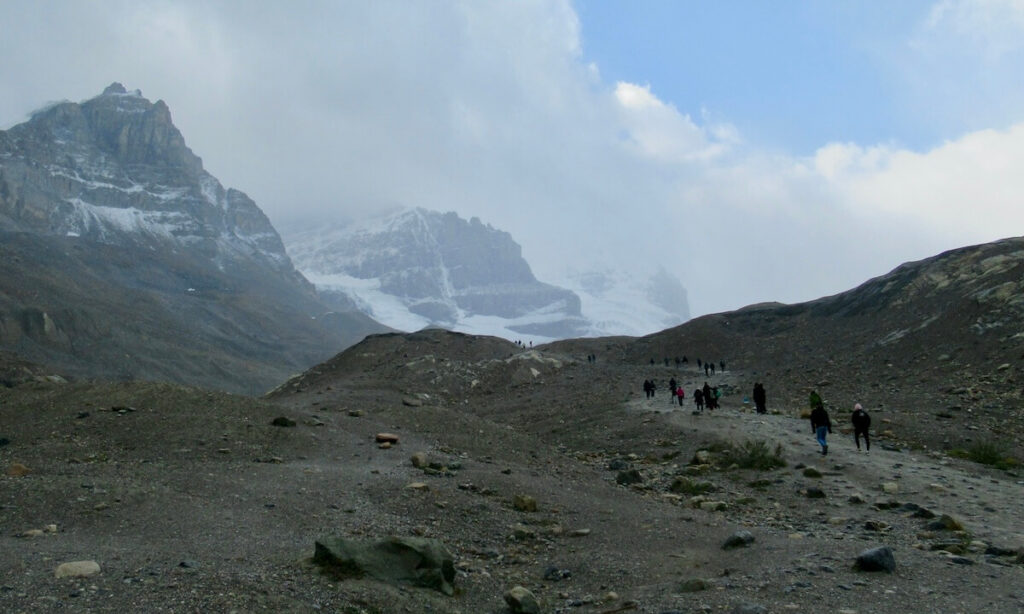 Athabasca Glacier - line of people walking up rocky path toward glacier on cloudy day