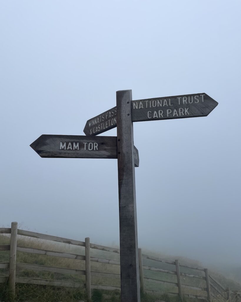 Wooden sign post for Mam Tor and National Trust Car Park on foggy day in Peak District