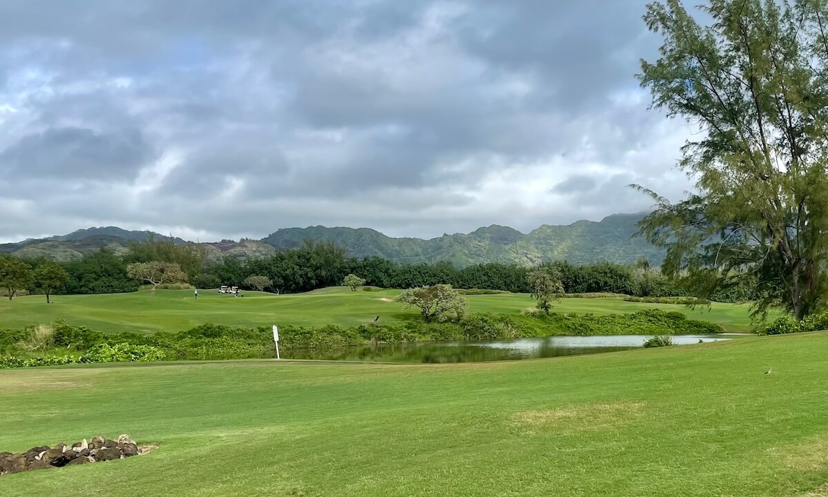 Poipu Bay Golf Course with golf cart on course, pond and lush green grass on cloudy day in Kauai