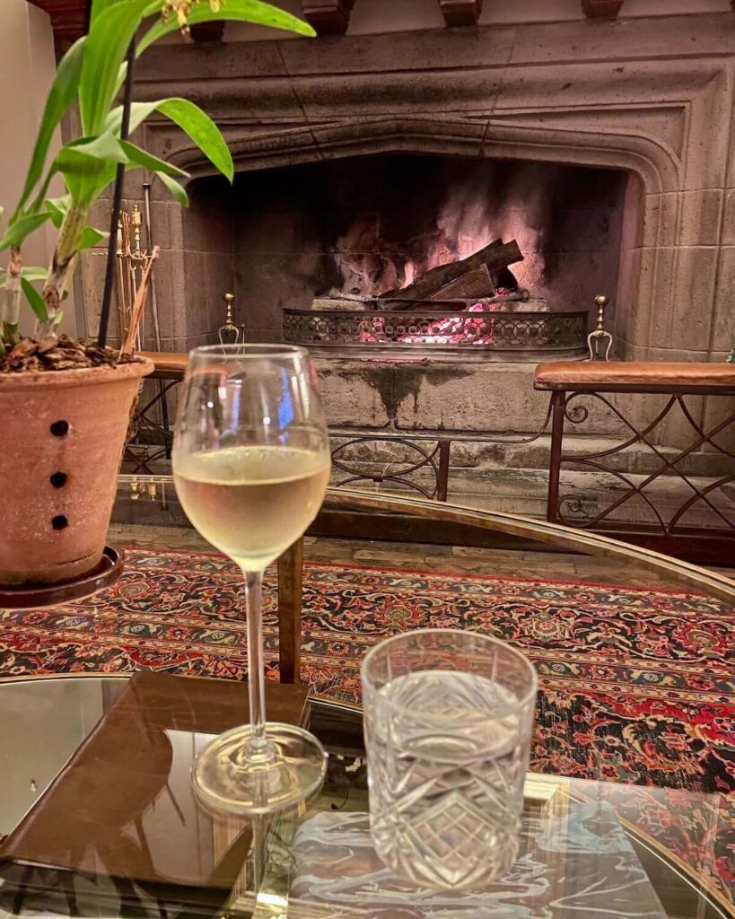 Glass of white wine and a water on a coffee table in front of a lit fire at Giraffe Manor
