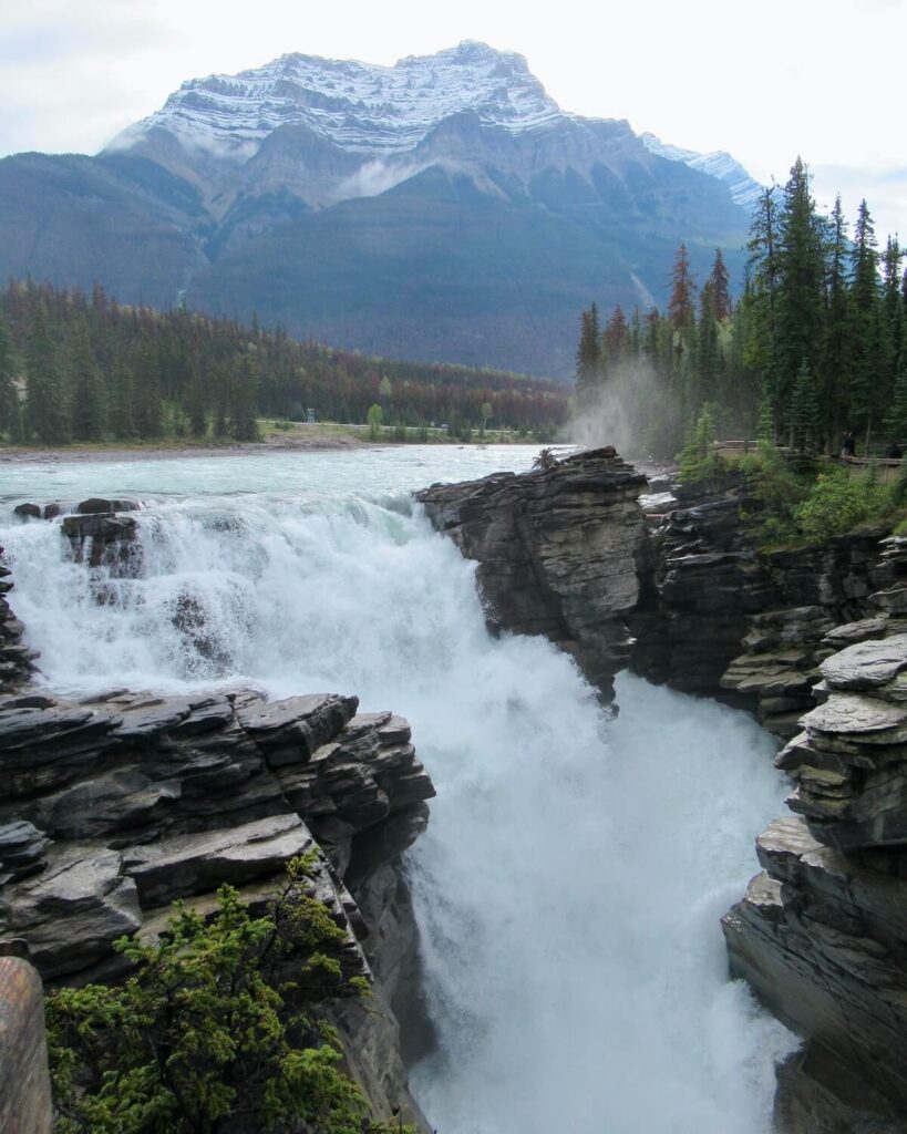 Athabasca Falls - powerfall falls witih slatted rocks and snow-topped mountains with grey sky