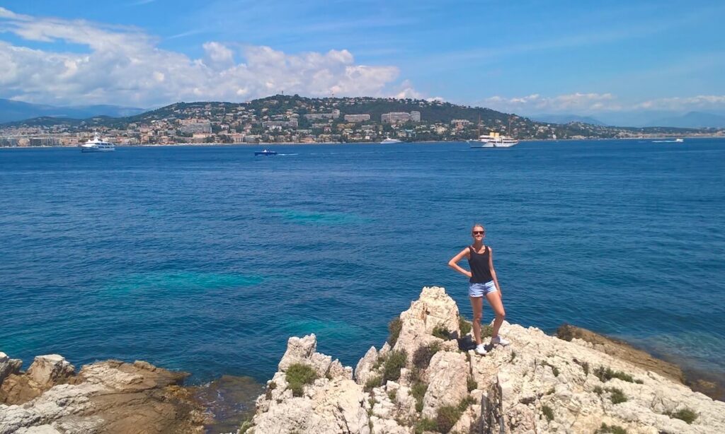 Samantha standing on rock on edge of Ile Sainte Marguerite on sunny day with view of Cannes