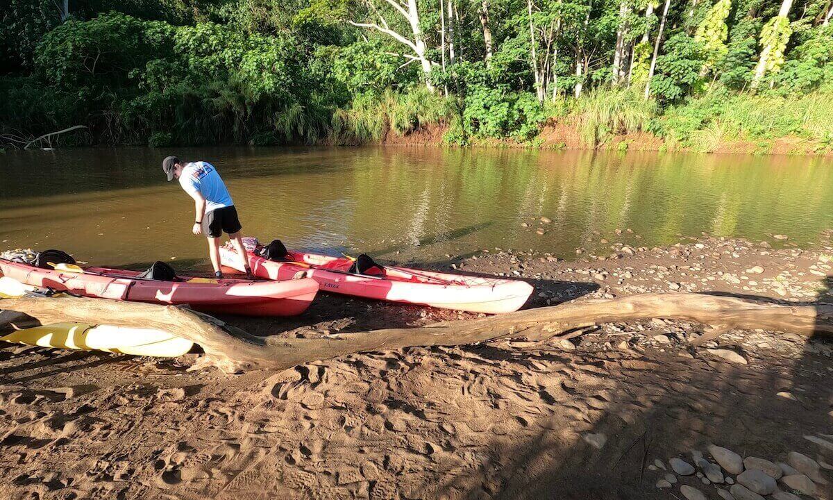 Man standing on beach landing pulling in red kayaks at Wailua River on the way to Secret Falls in Kauai