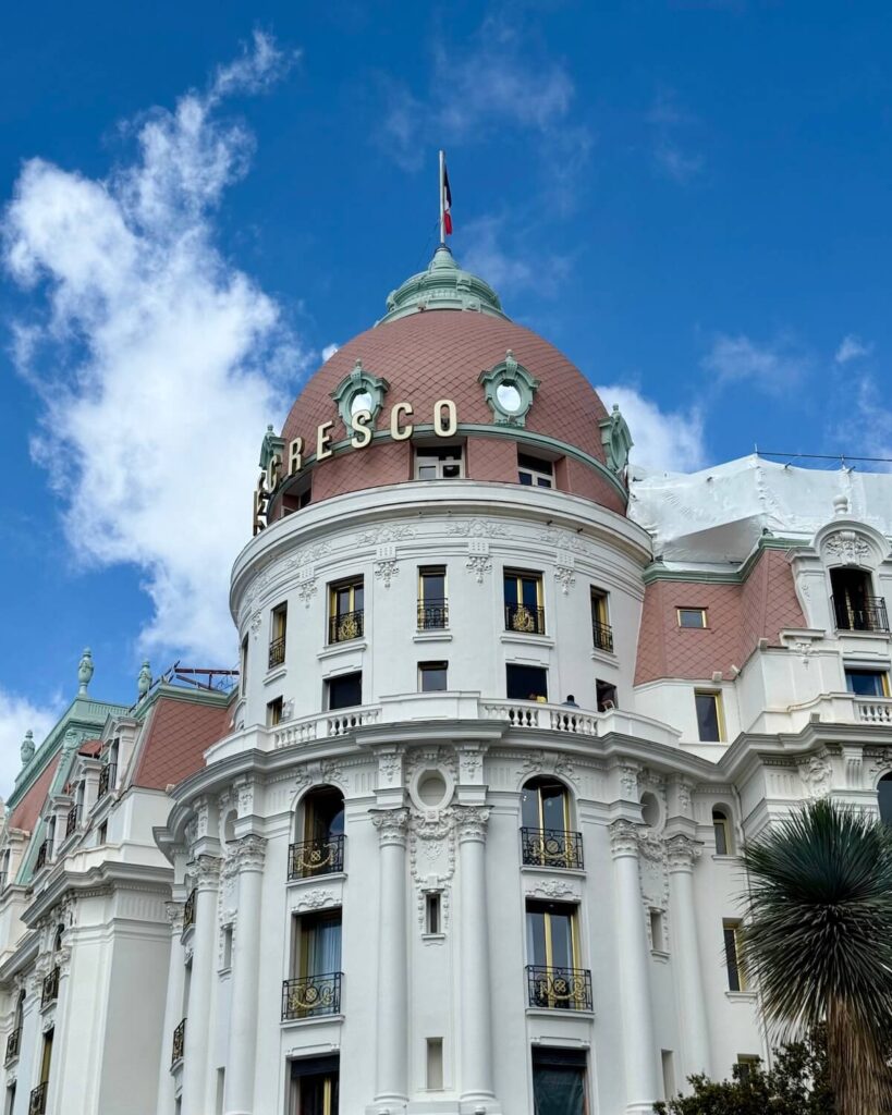 Le Negresco hotel in Nice with pink dome roof and green markings with blue sky and palm trees