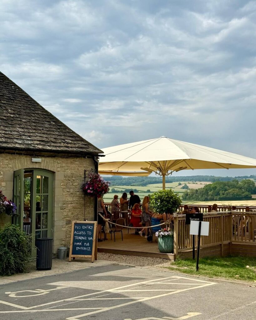The Farmer's Dog pub with large yellow umbrella and countryside view from the bustling terrace