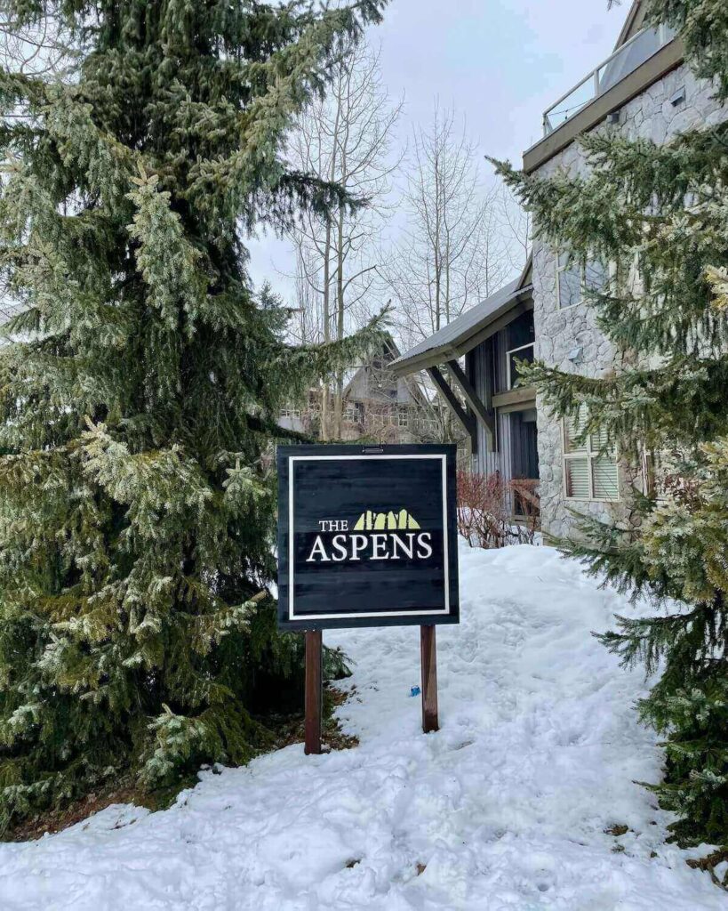 The Aspens sign outside Blackcomb ski in ski out accommodation with trees and snow on the ground