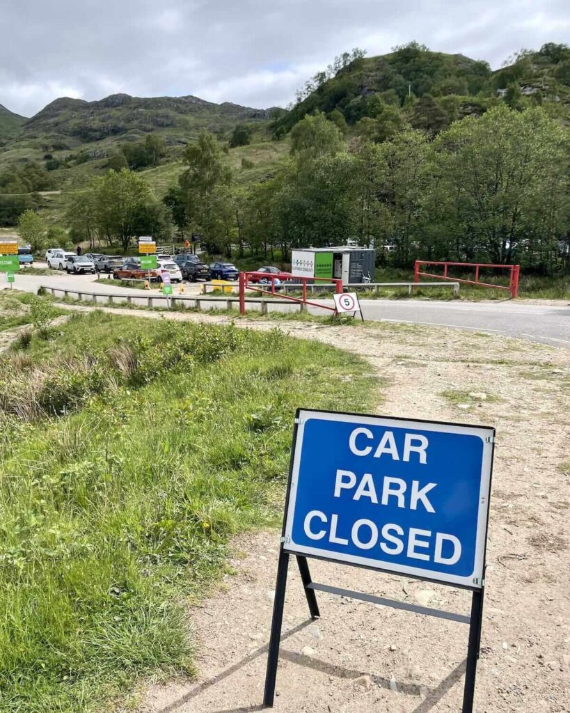 Glenfinnan Community Car Park - blue sign reading Car Park Closed and cars parked in the distance