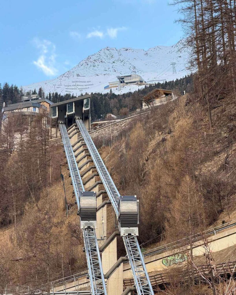 Funiculars going up and down hill in Solden towards ski resort with snow only at top of mountain