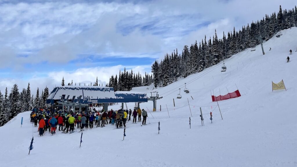 Lines at chairlifts at 7th Heaven Express with small crowd of people waiting at Whistler Blackcomb