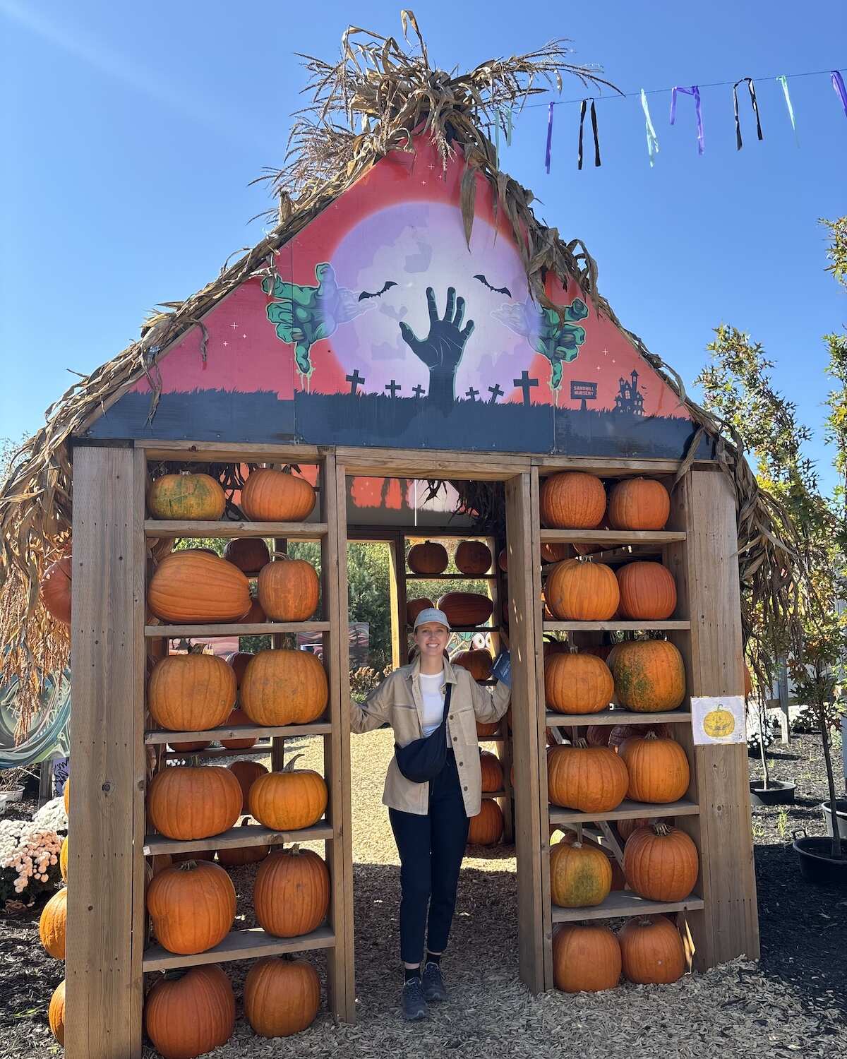 Samantha standing in the frame of a house made of pumpkins Halloween display at Sandhill Farm in Huntsville