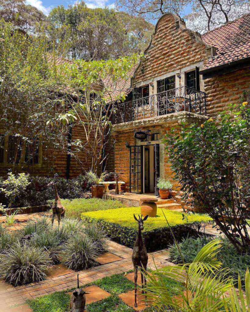 Grounds at Giraffe Manor with brick building, leafy gardens, giraffe statues and bright green hedges