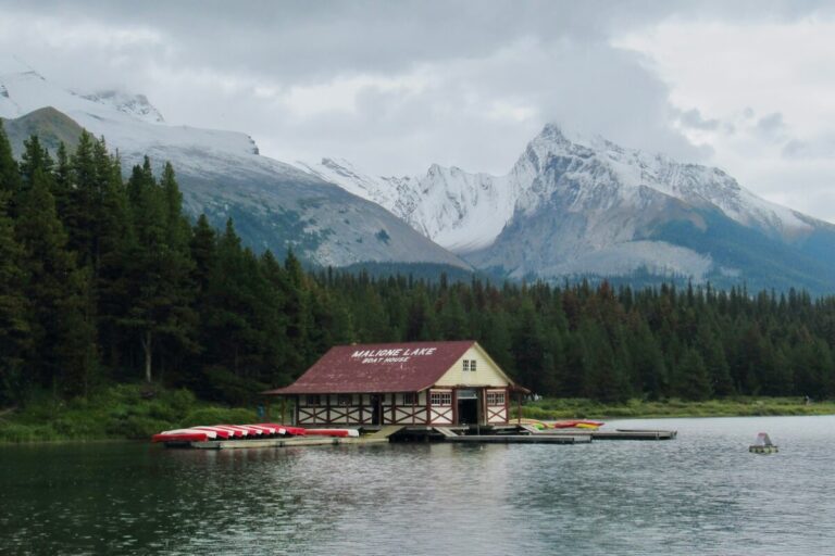 Maligne Lake Boat House and canoes on lake with snowy mountains and pine forest behind on cloudy day
