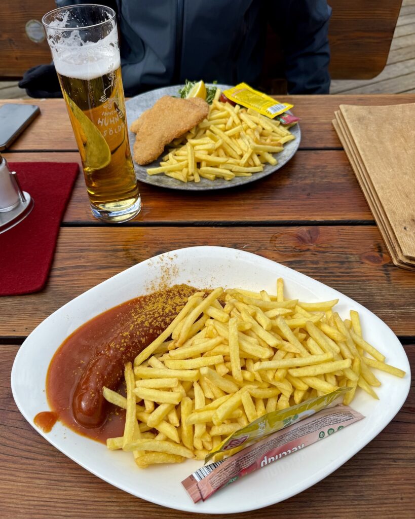 Curryworst and fries and schnitzel and fries on wooden table and a beer at Annemaries Hühnersteign