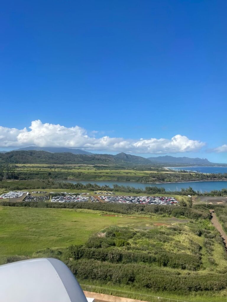 Flying out of Lihue airport for 10 days in Kauai - showing grassy area, car park, ocean and hilly ranges