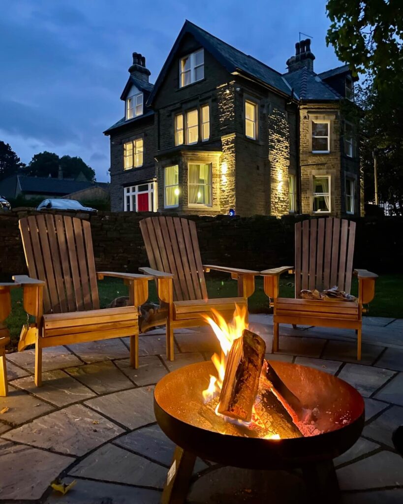 Large stone house and a pointed roof with a lit fire pit in the garden at night in the Peak District