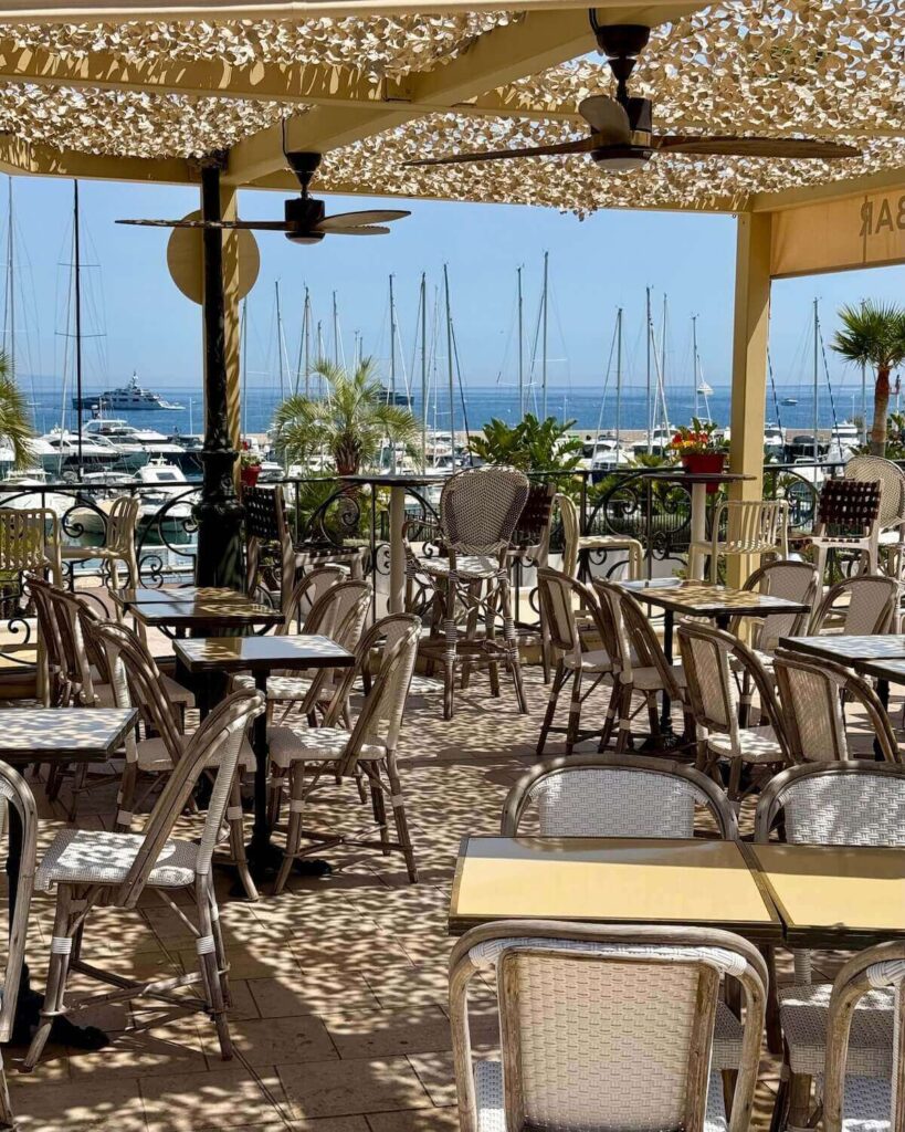 Outdoor terrace restaurant in Saint Jean Cap Ferrat on sunny day with view of harbour and palm trees