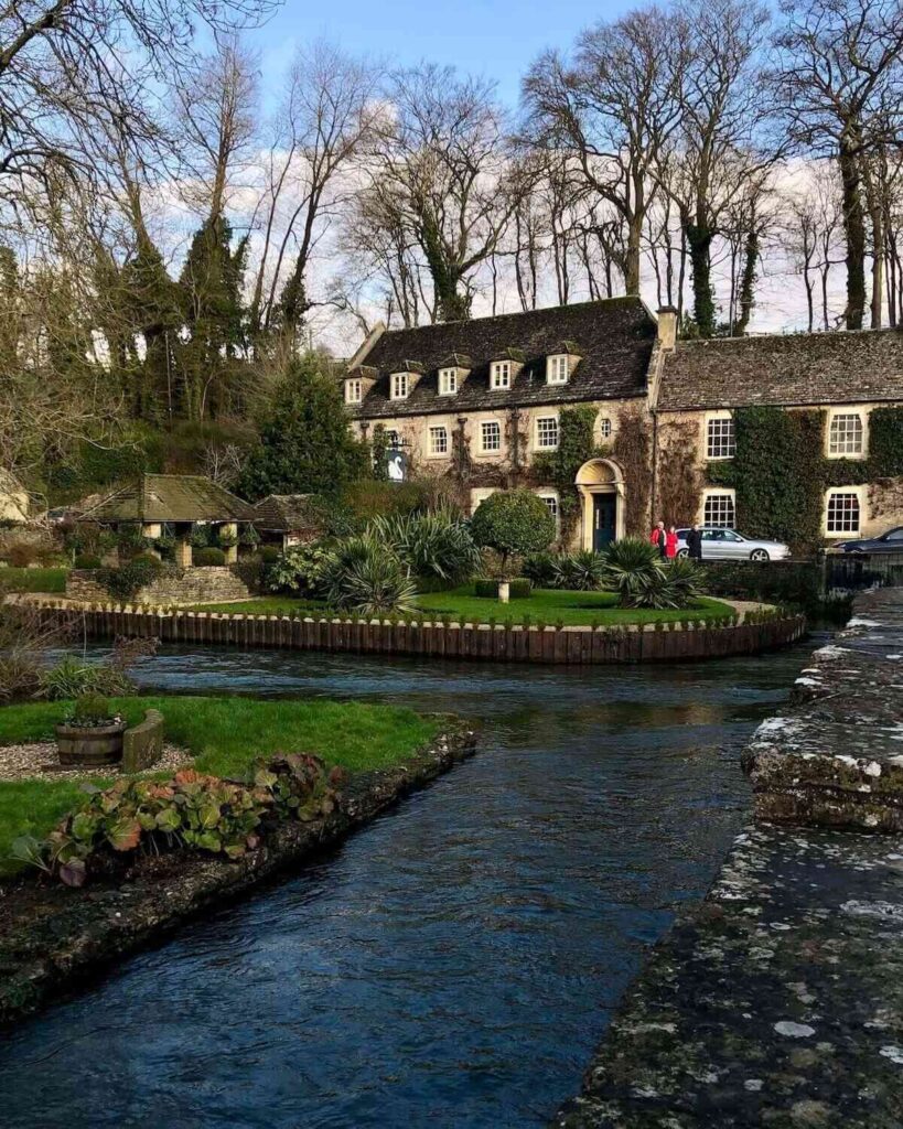 Bibury trout farm - stream around grassy island with ivy covered brick cottages with bare winter trees