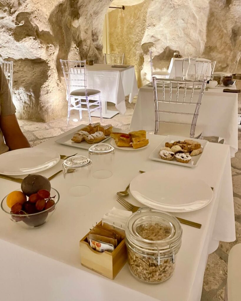 Breakfast at Palazzo Del Duca hotel in Matera - plates of food on white tablecloth in white-walled cave