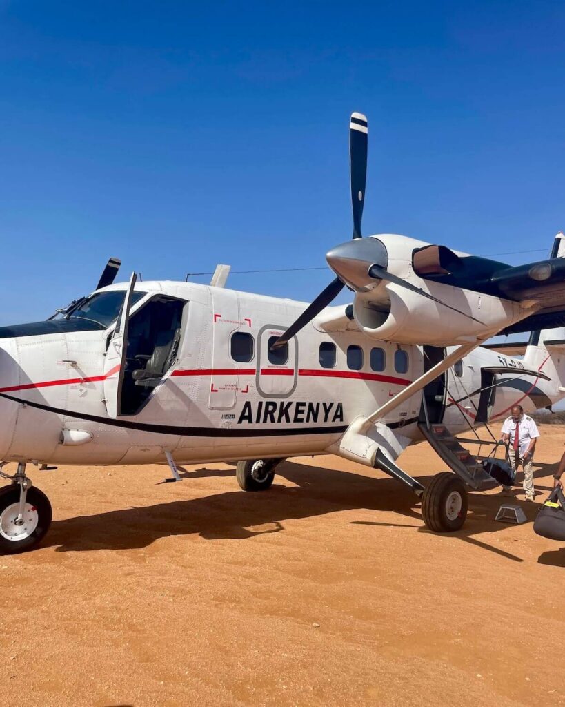 AirKenya plane on safari landing strip with man loading safari luggage onto plane with bright blue sky