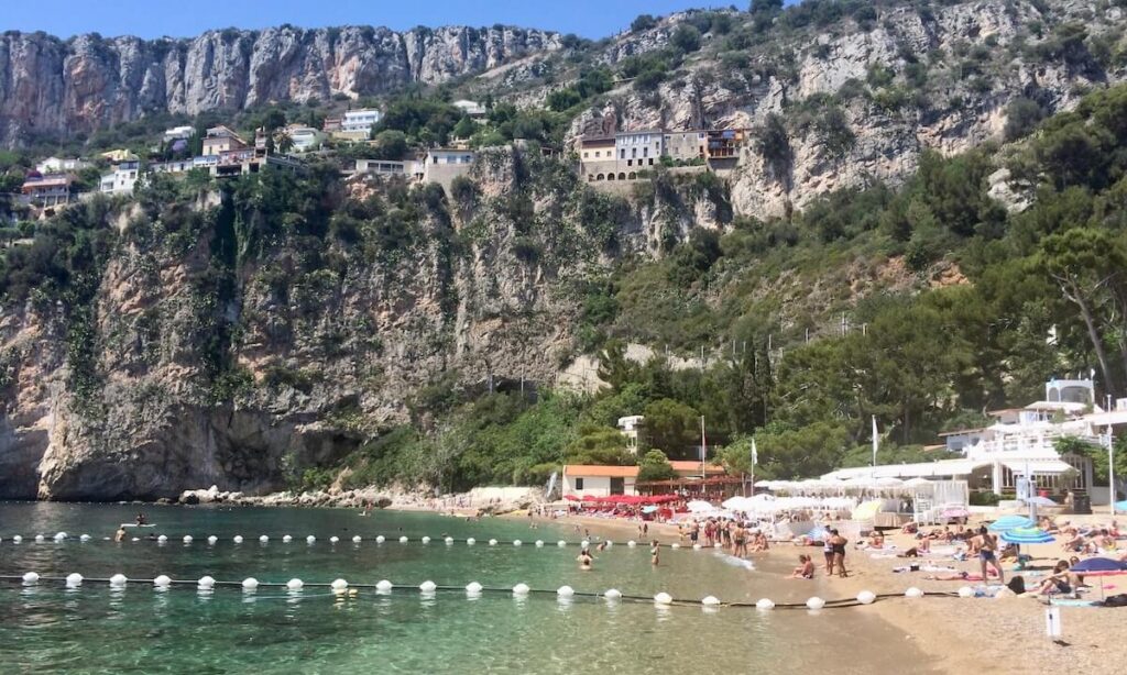 Plage Mala Cap D'Ail - beach with separated area for club and public nestled in cove with houses on cliffs