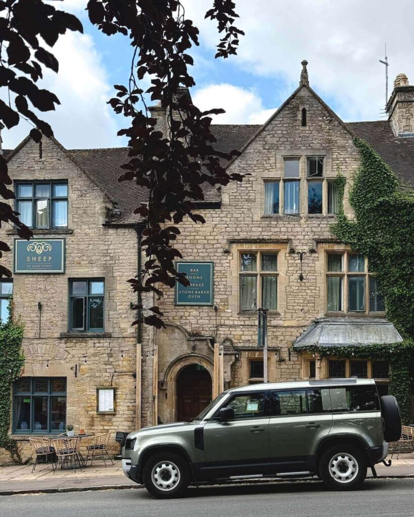 Old brick building called The Sheep Restaurant on slanted hill with large car in front in Stow on the Wold
