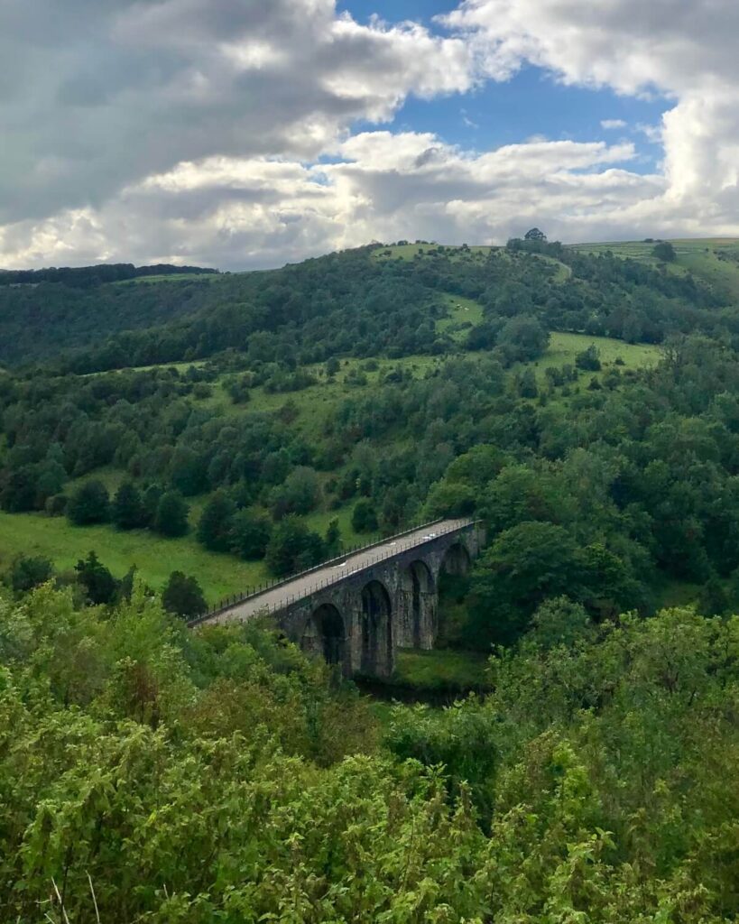 Monsal Viaduct from Monsal Head viewpoint with countryside and trees surrounding the bridge on cloudy day