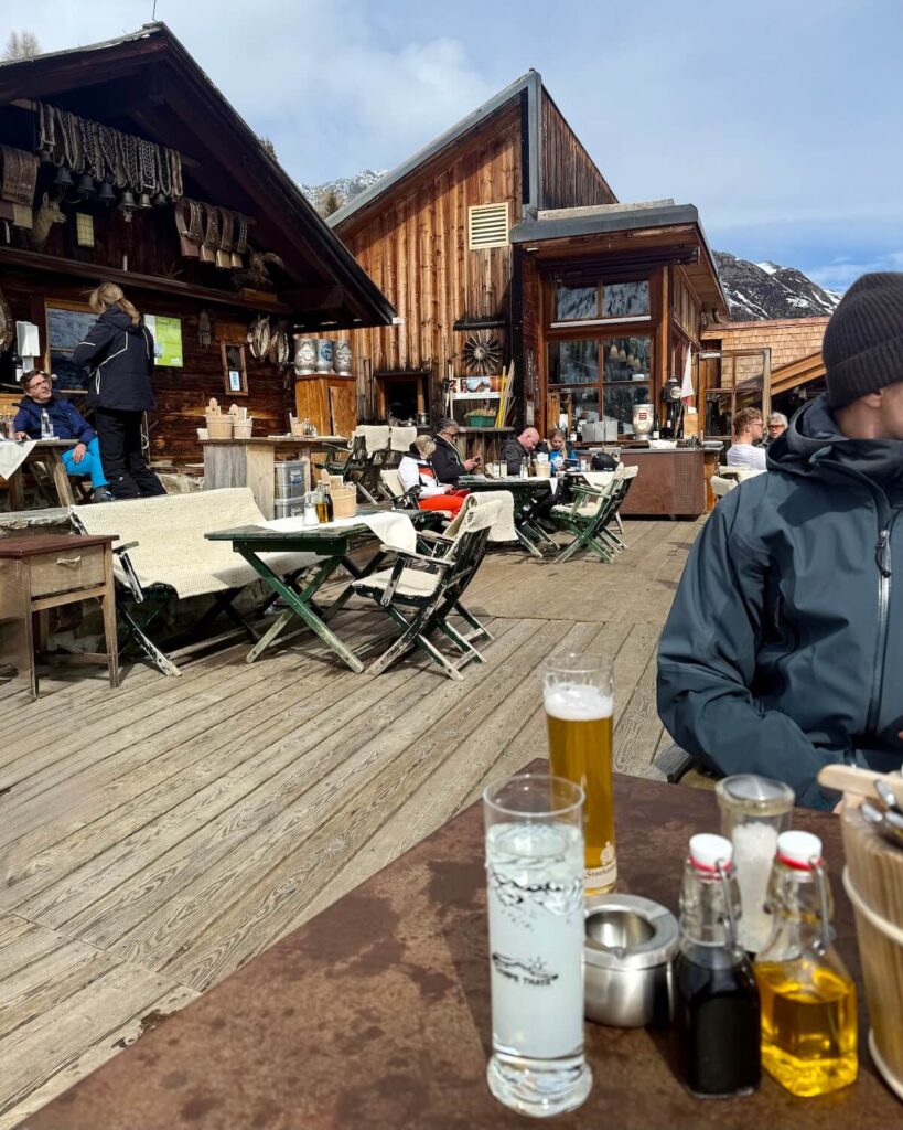 Terrace at Almwirtschaft Gampe Thaya in the sun with customers at tables in ski gear at Solden Ski Resort