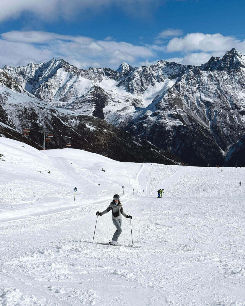 Samantha standing on skis in middle of slopes on sunny day with vast mountain range behind in Solden Austria