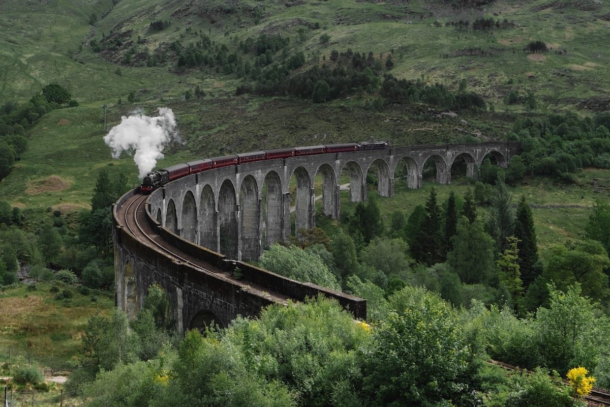 Glenfinnan Viaduct Viewpoint with Jacobite Steam Train passing across blowing steam with a green tree-filled landscape