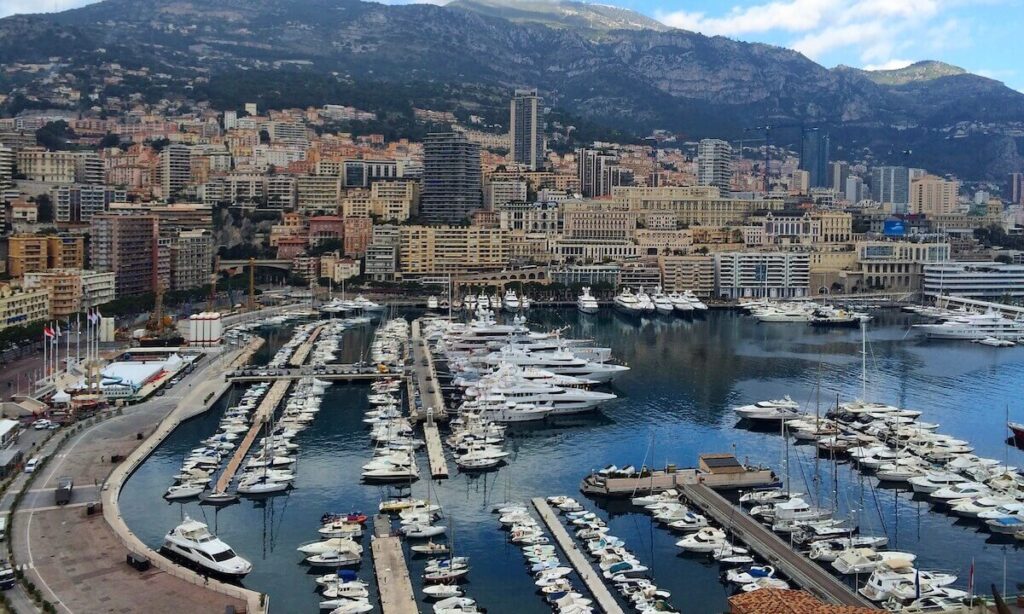 Monaco harbour with small boats and large yachts with yellow buildings around port and mountainous backdrop