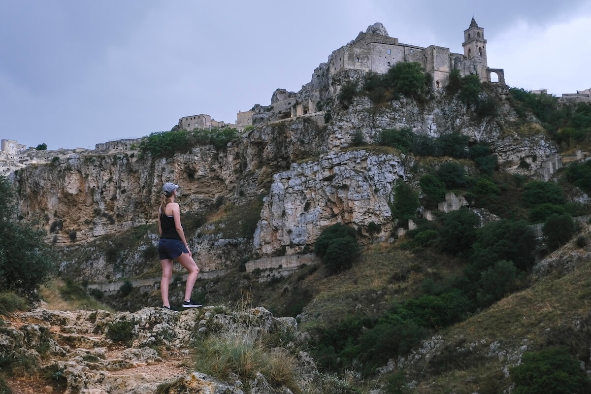 Samantha standing on rock looking out to church on top of rocky hil in Matera - Hike to be included on a Matera itinerary