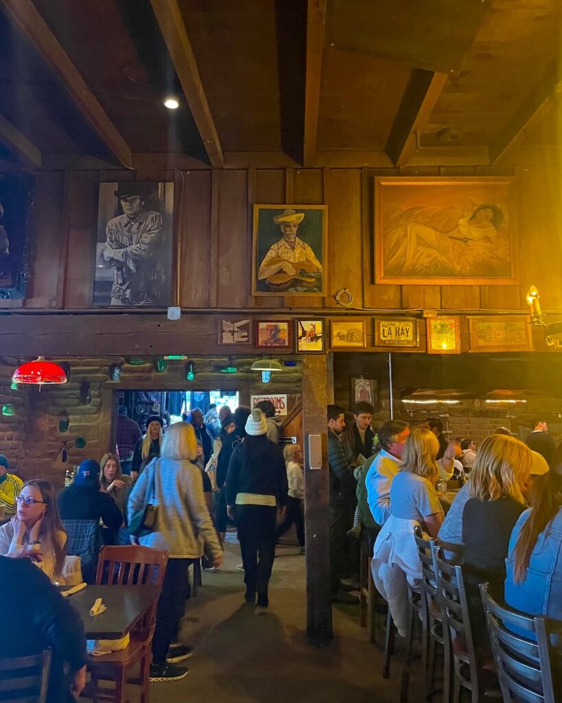 Interior of bar at Pappy & Harriet's with people sitting at bar and at tables. Painting of musicians on the wall