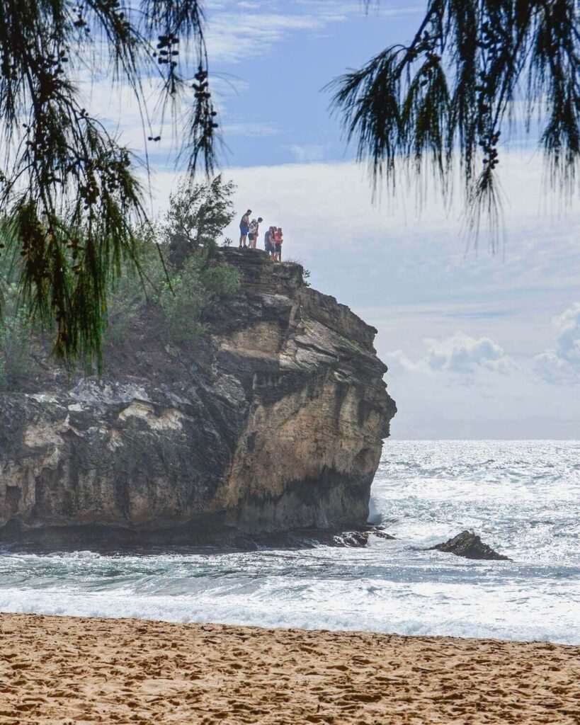 People standing on cliff edge at Keoneloa Bay on Shipwreck Beach in Poipu with water lashing below on the beach