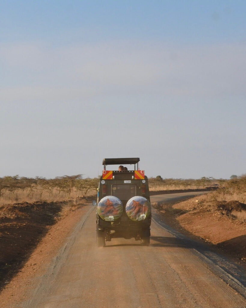 Safari jeep driving into Nairobi National Park at the entrance with the roof popped and people looking out Kenya