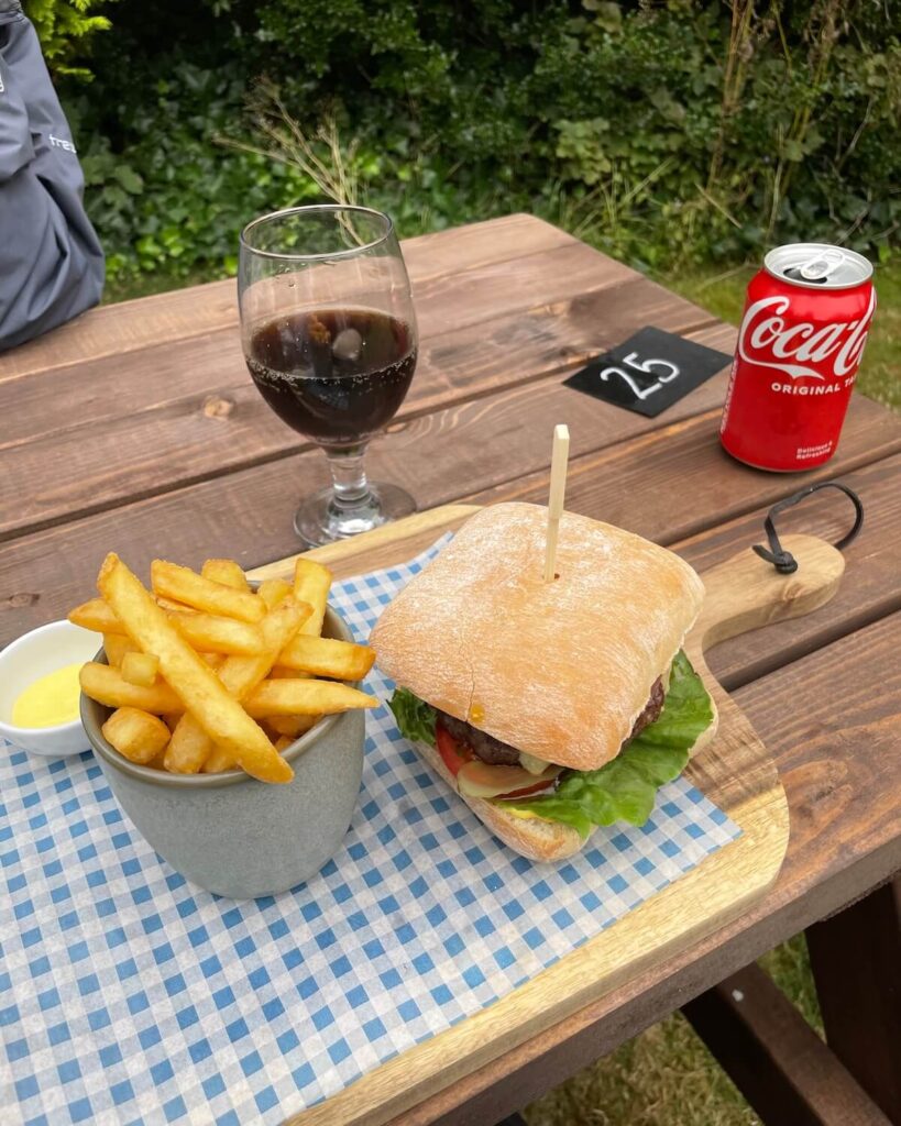 Burger and chips served on wooden plank with coke can on wooden picnic bench at Rose Cottage Cafe in Castleton