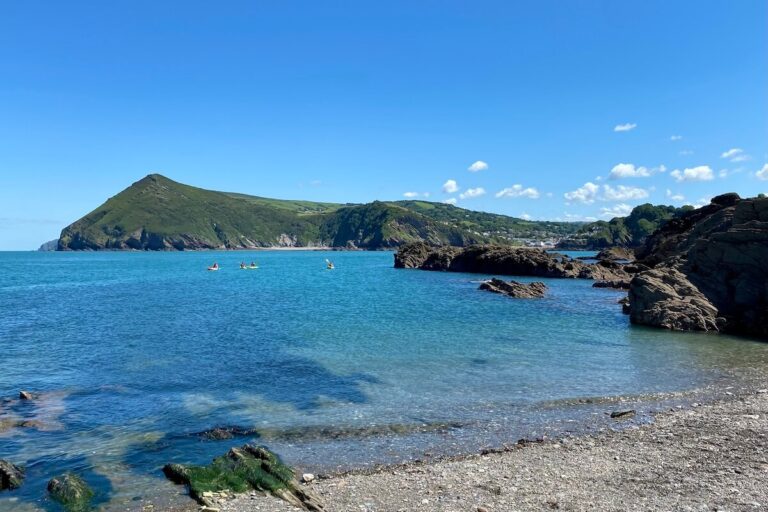 Beach in Ilfracomb with blue sky, rocky beach, bright blue sea and countryside in backdrop - Devon is one of the best long weekend breaks in the UK