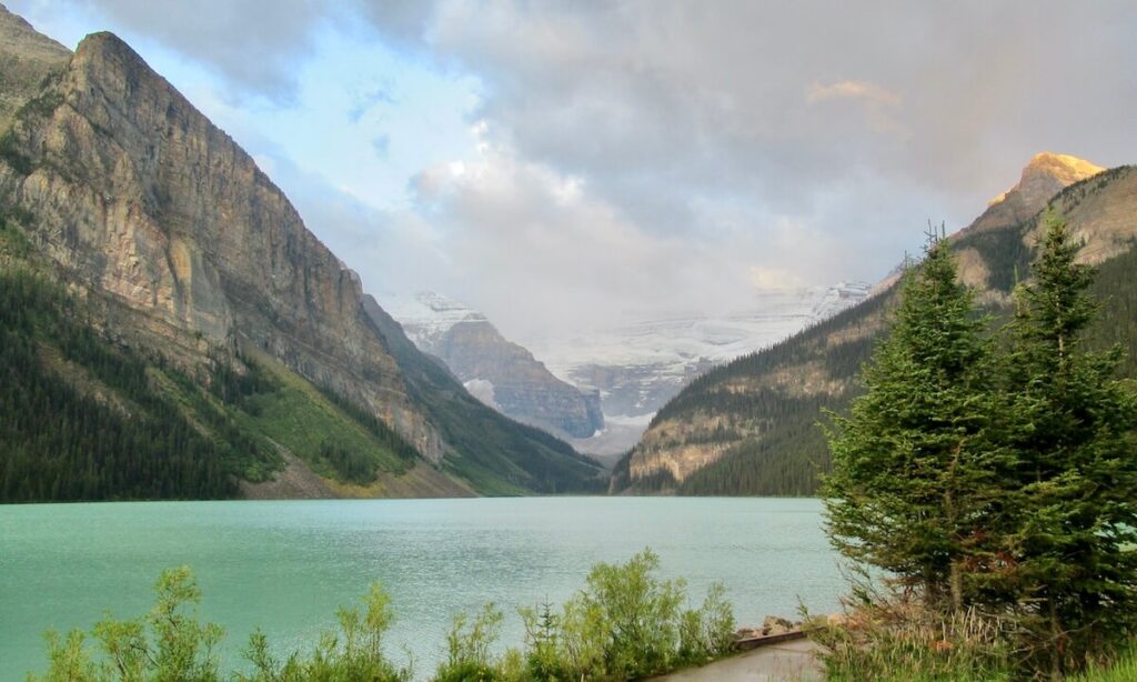 Lake Louise at sunrise with golden clouds on top of mountains and snow covering with bright green lake and cloudy sky
