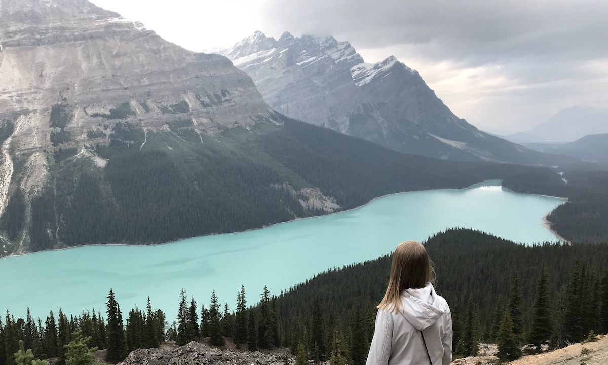 Peyto Lake - green lake in the shape of wold with light snow on mountains next to lake and Samantha with back to camera looking at lake on Icefields Parkway