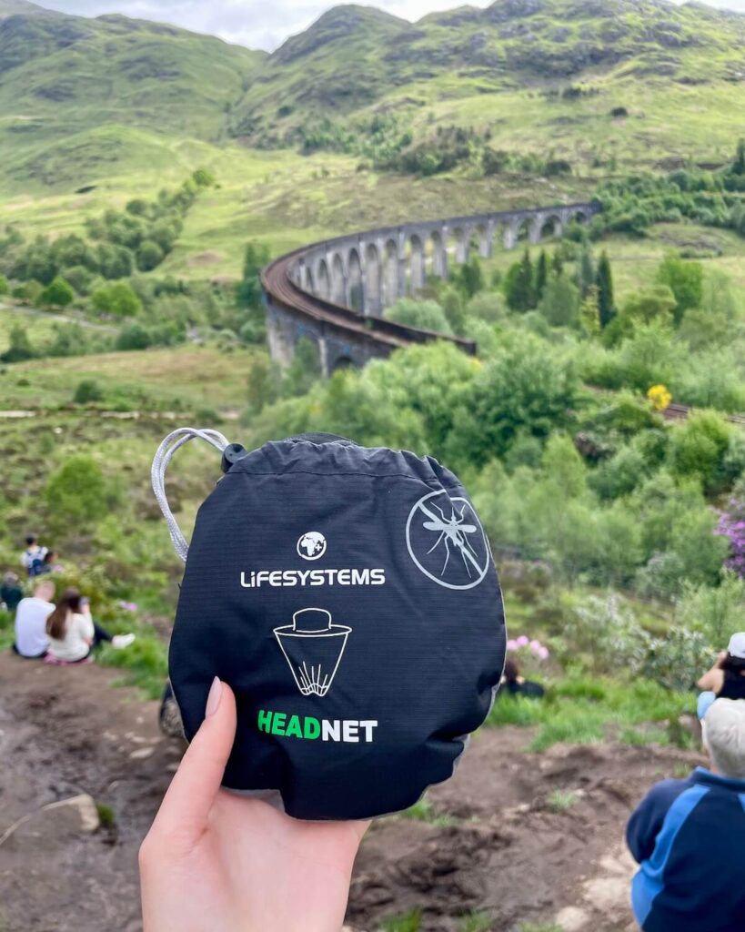 Lifesystems head net used for midges in Scotland in its case held up against the backdrop of Glenfinnan Viaduct
