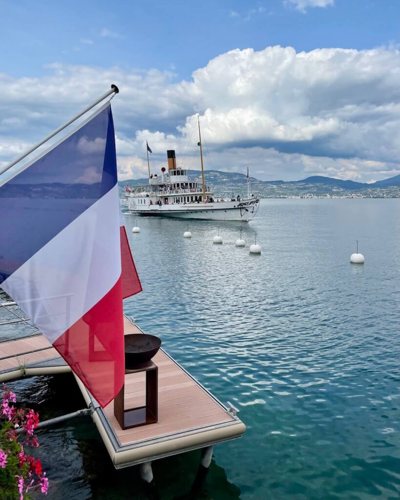 Boat tour is one of the best things to do in Yvoire - boat on Lake Geneva with French flag in foreground and cloudy sky